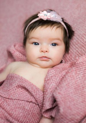Baby wearing pink headband lies on pink knit blanket during portrait session.