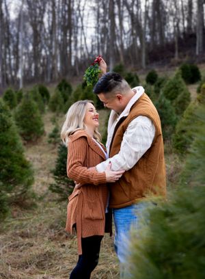 Couple sharing a romantic moment among evergreen trees at a Christmas tree farm.