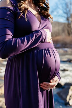 Close up of pregnant belly in purple maternity dress against winter landscape.