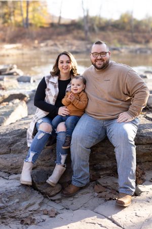 Family of three sitting together on rocky terrain during golden hour.