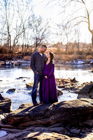 Couple stands on rocky outcrop by frozen river in winter landscape.