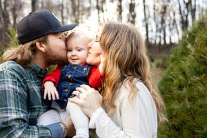 Parents kiss baby in winter clothing during outdoor family portrait session.