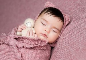 Sleeping baby wrapped in pink knit blanket with small plush toy.