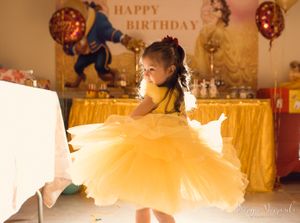 Young dancer twirls in a flowing yellow princess dress at a birthday party with golden decorations.