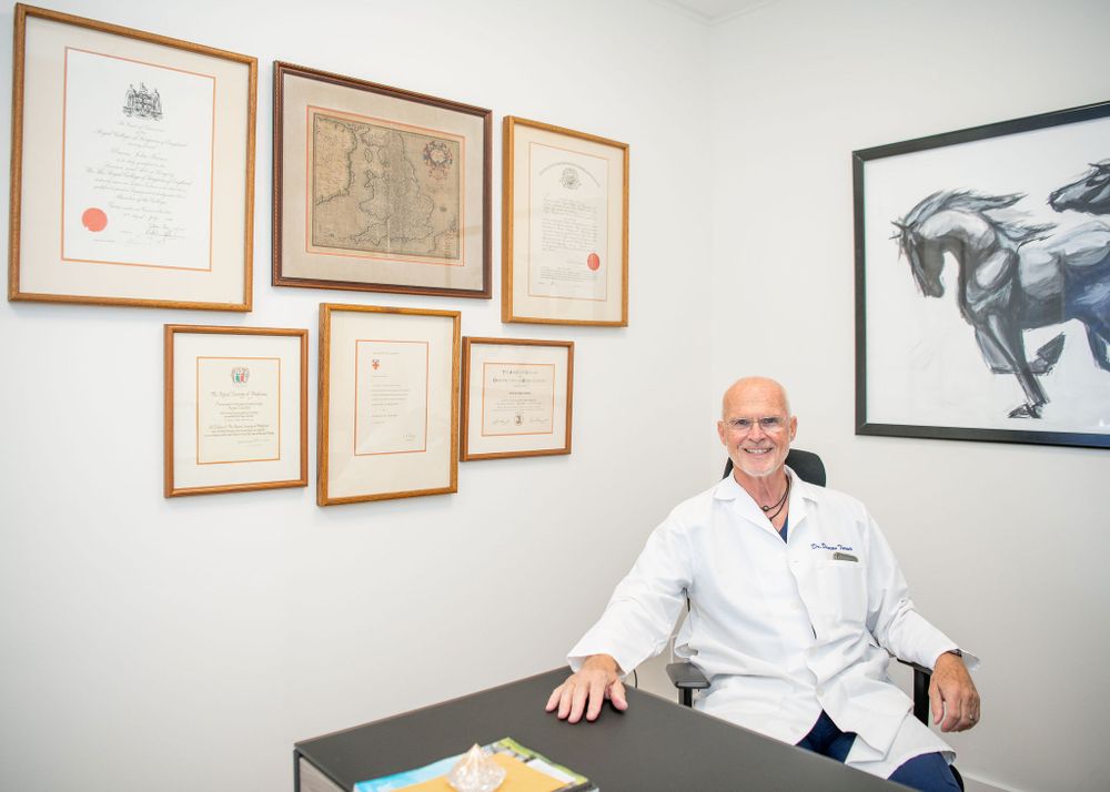 doctor sitting at his desk with his awards and accomplishments framed on the wall behind him