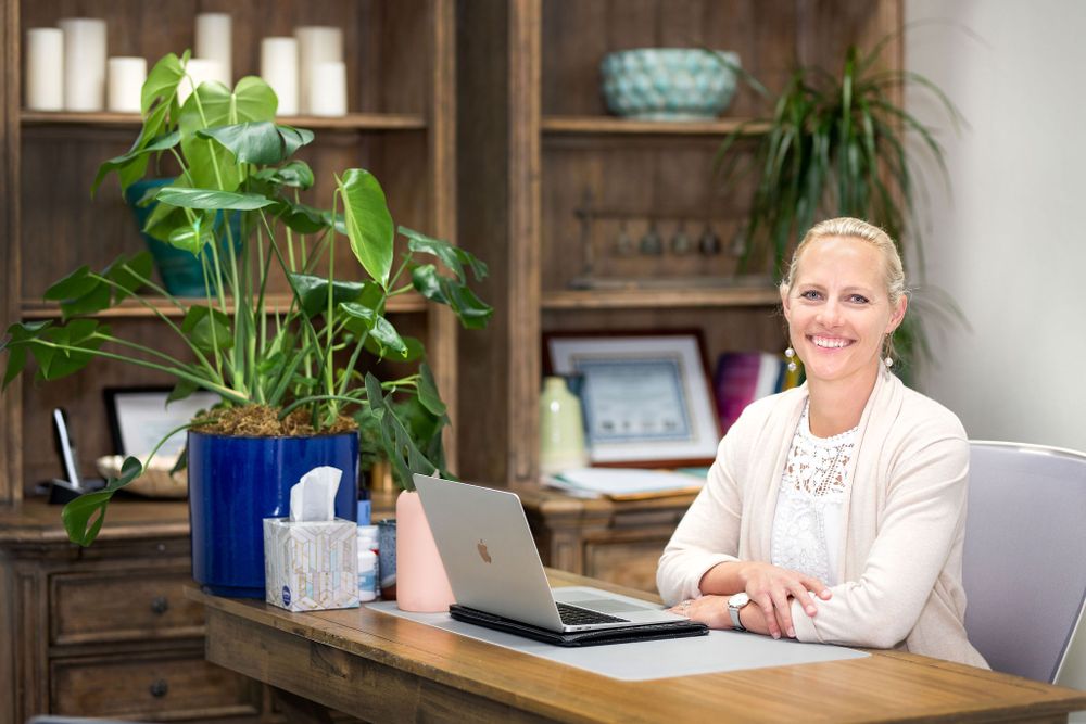 woman smiling at the camera sitting at her desk in her office with bookshelves behind her