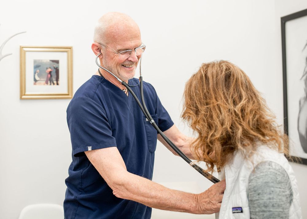 doctor smiling at patient while listening to her heart with his stethescope