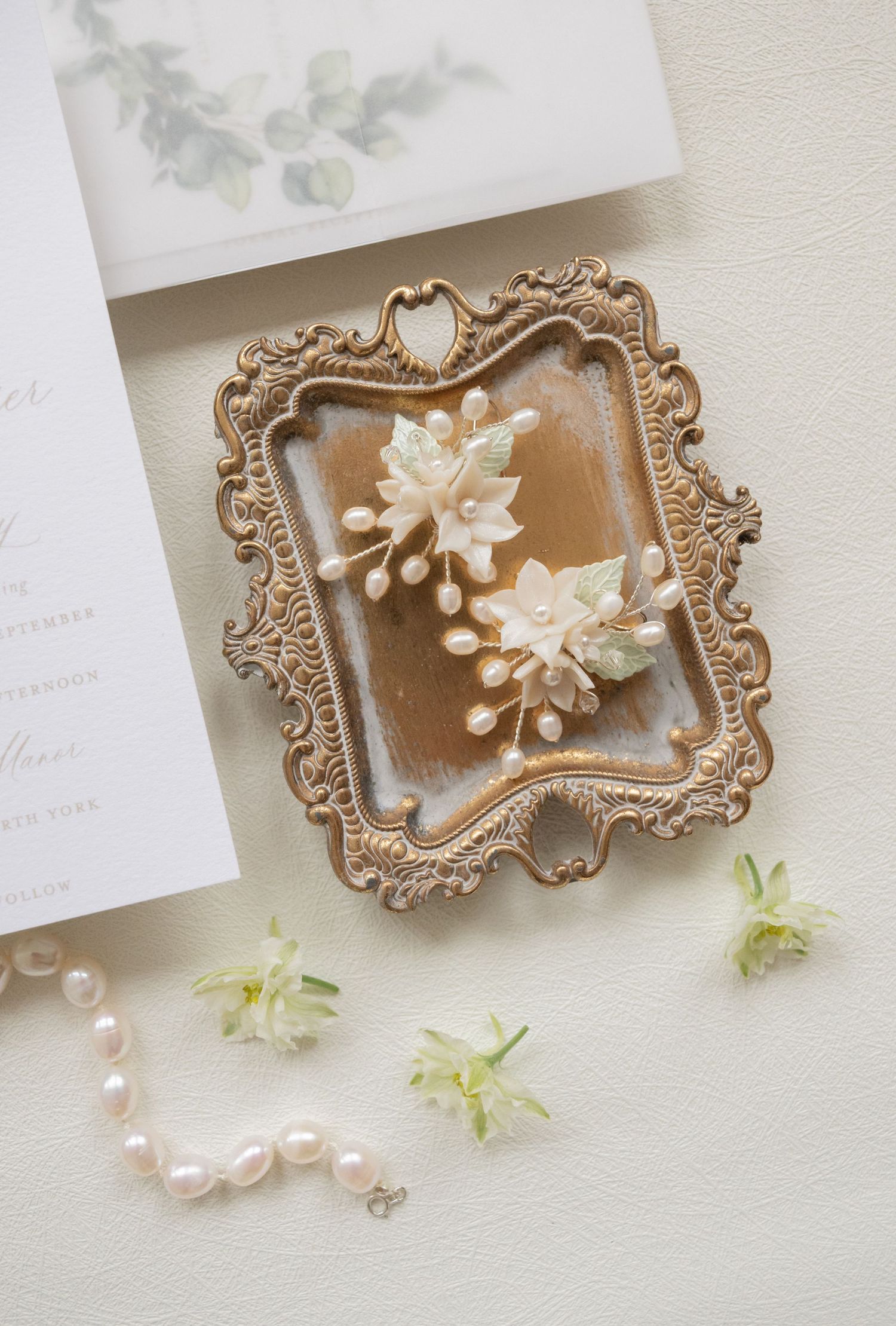 Ornate gold frame with floral design displayed with wedding stationery and pearl details.