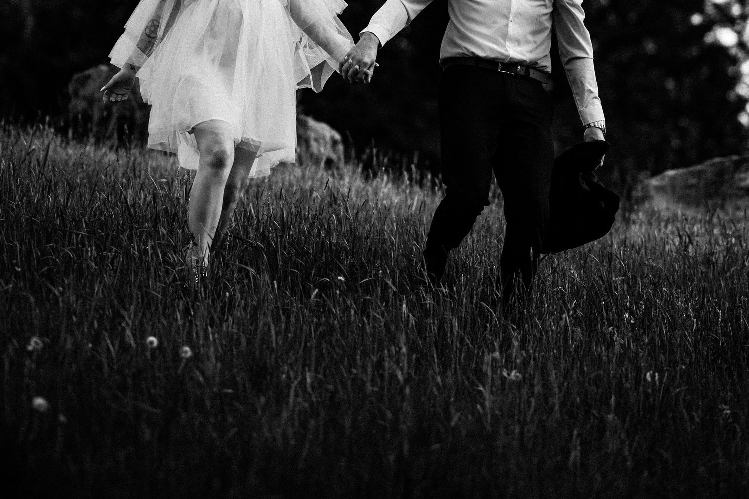 Black and white photo of legs walking through tall grass in formal attire.