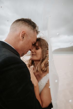 Intimate wedding portrait showing tender moment on a cloudy beach.
