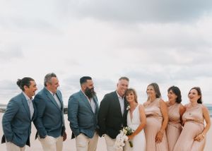 Wedding party in gray suits and blush dresses posing for photos on a beach.