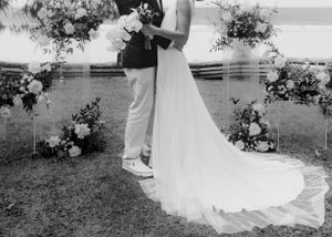 Black and white photo of a wedding ceremony under a floral arch beside a lake.