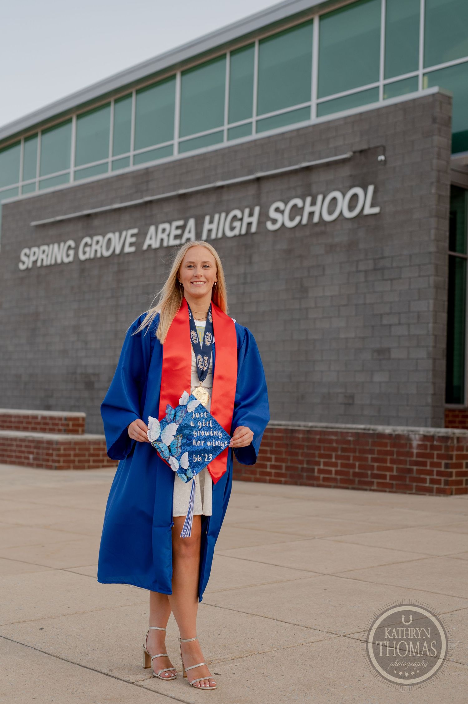 Graduate holds decorated cap in front of Spring Grove Area High School wearing blue and red regalia.