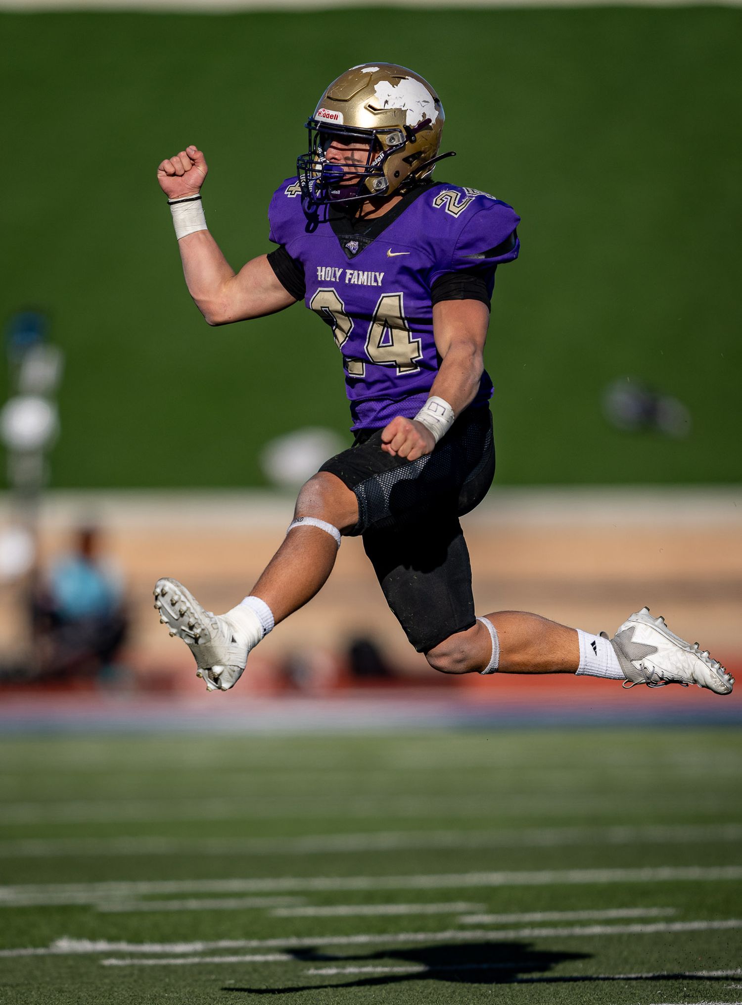Football player in purple uniform leaping mid-air with fist raised in celebration.