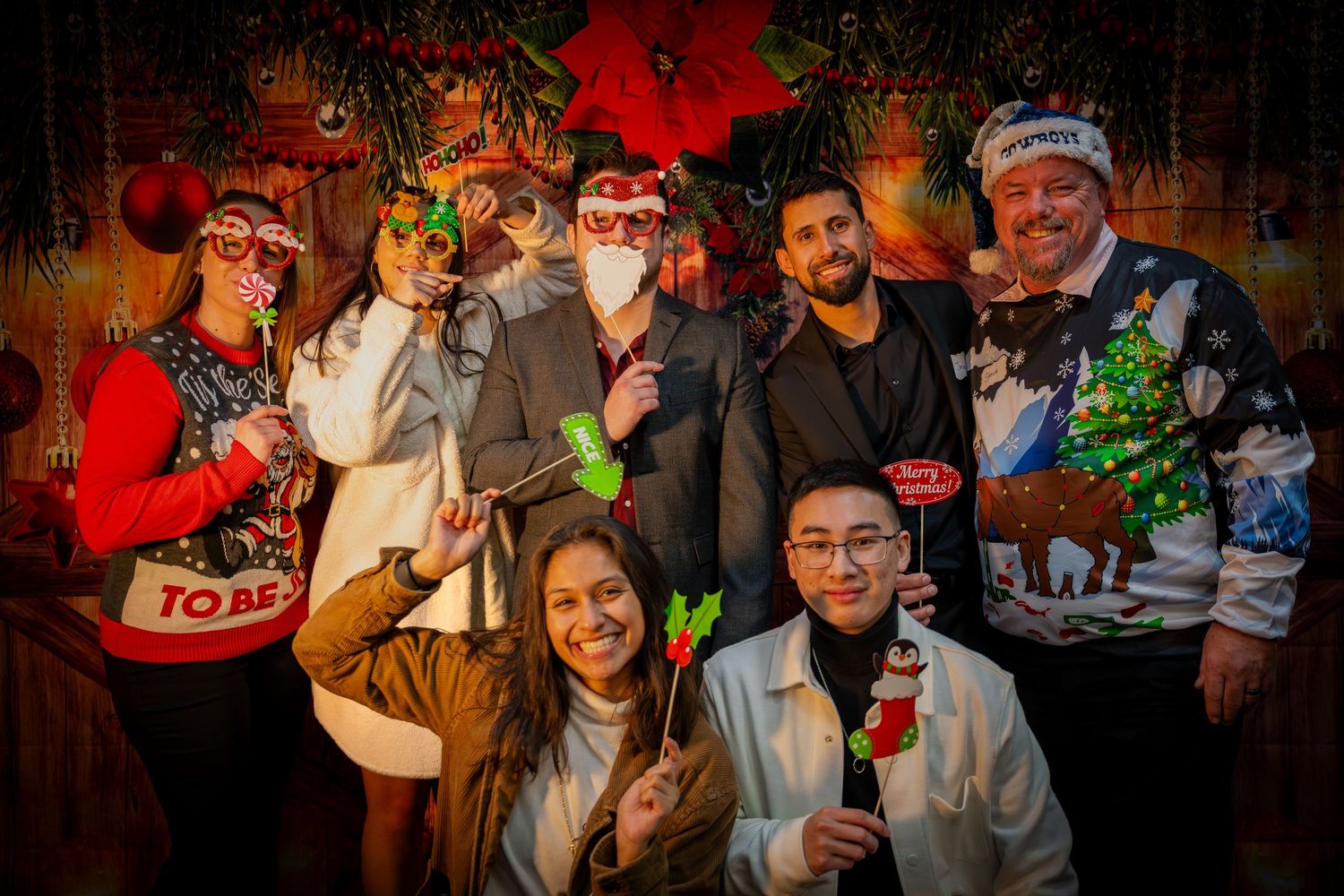 Celebration gathering with multiple people posed in front of decorative holiday backdrop.