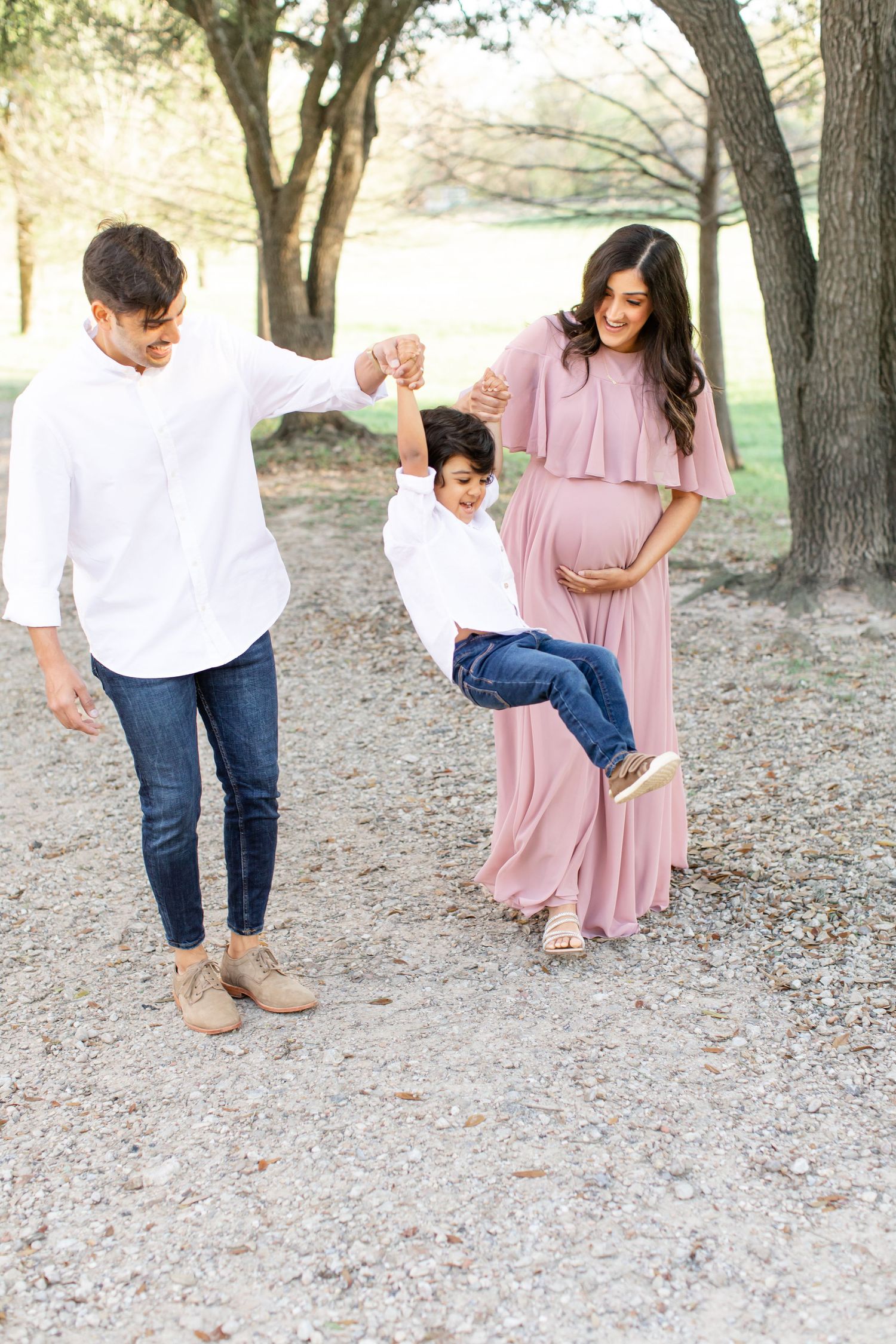 A playful family moment as parents swing their young child between them on a park path.