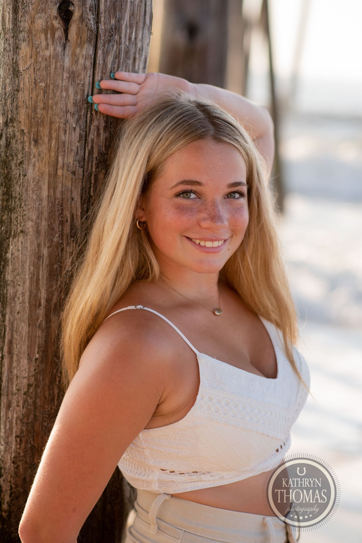 Summer portrait against weathered wooden pier post with natural beach lighting.