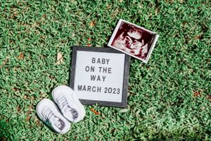 Ultrasound photos and pregnancy announcement signs laid out on green grass.