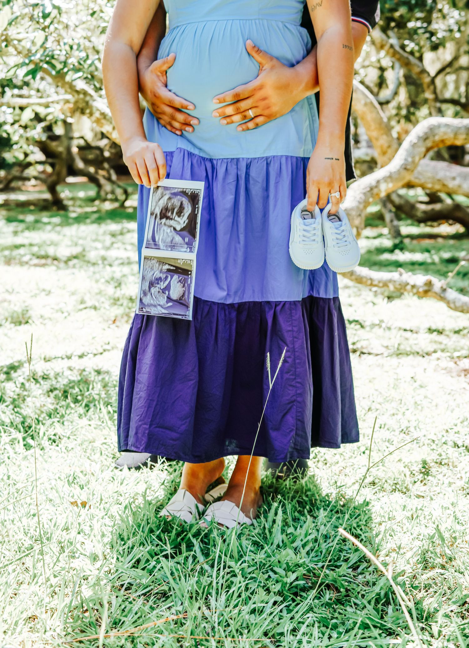 Close-up of hands holding ultrasound photos while wearing blue and purple outfits.
