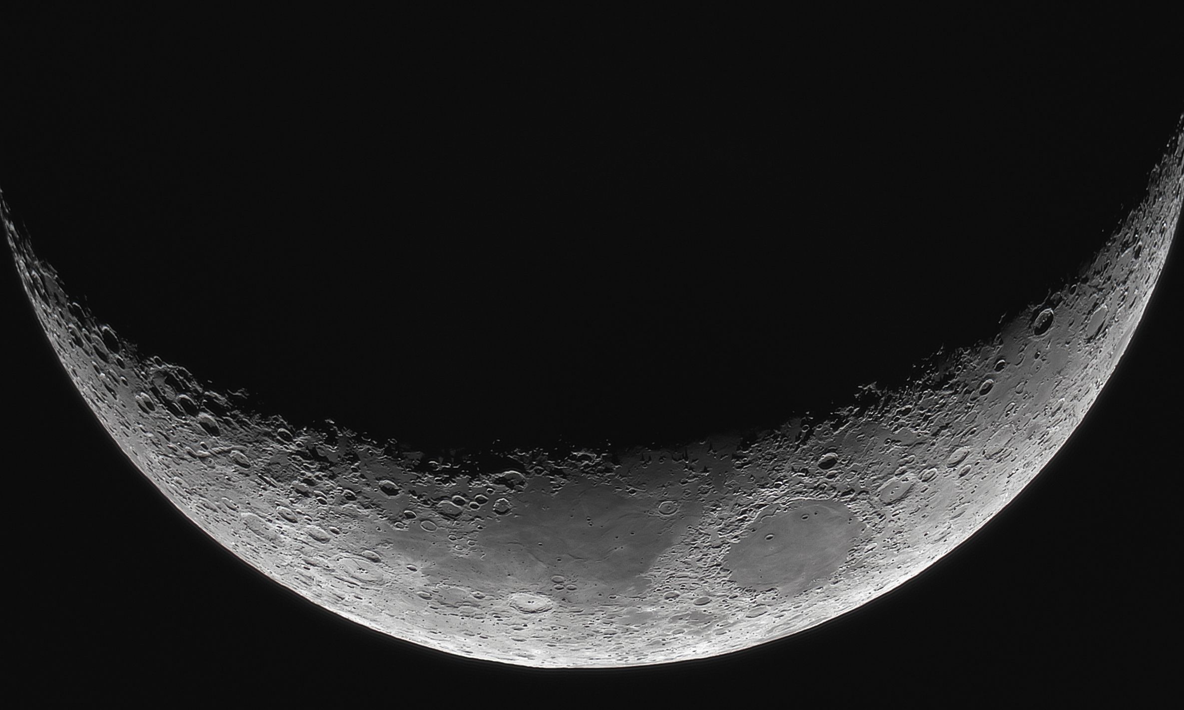 Detailed black and white photograph of a crescent moon showing lunar surface features.