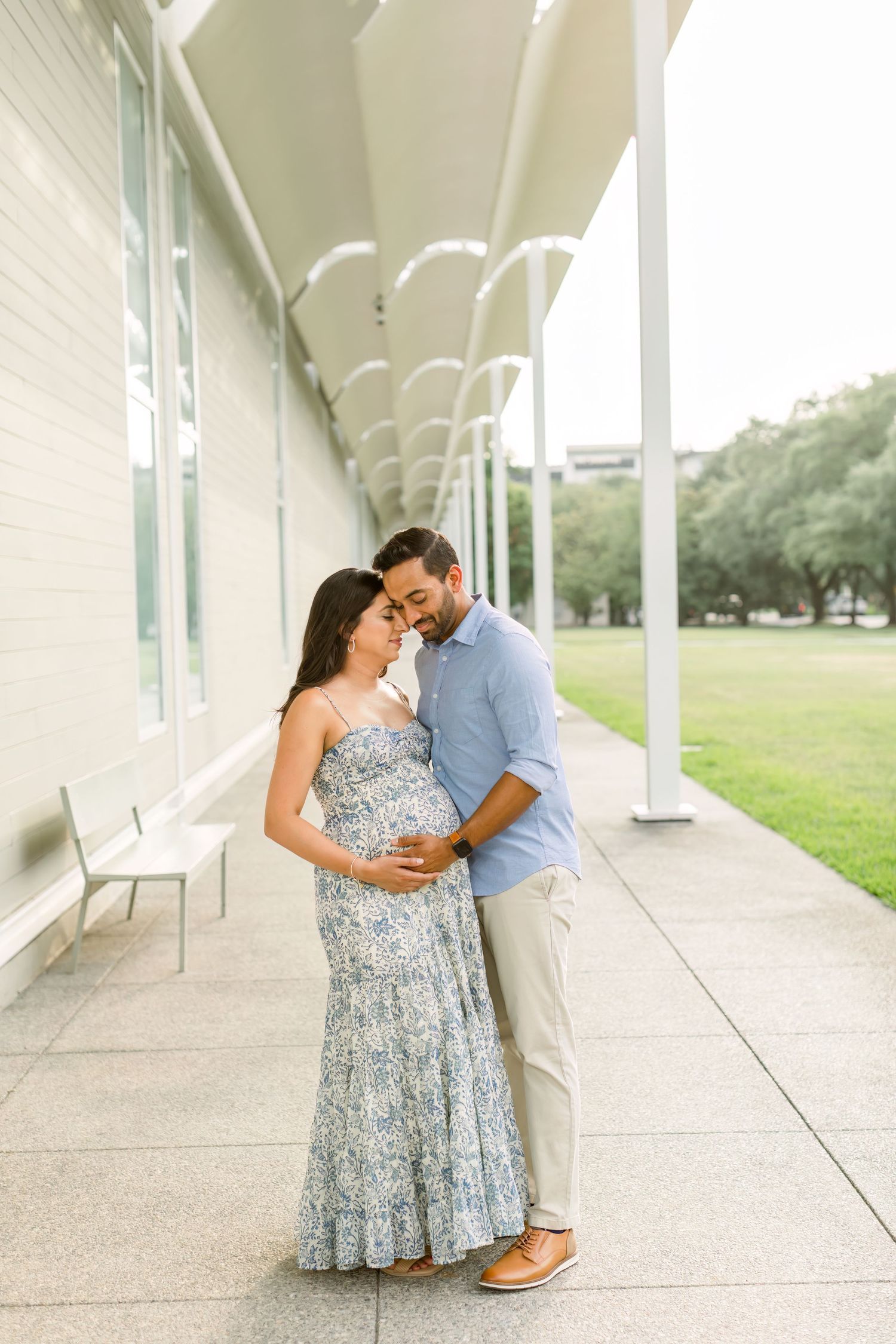 A couple embraces on a covered walkway, wearing a floral maxi dress and blue shirt.