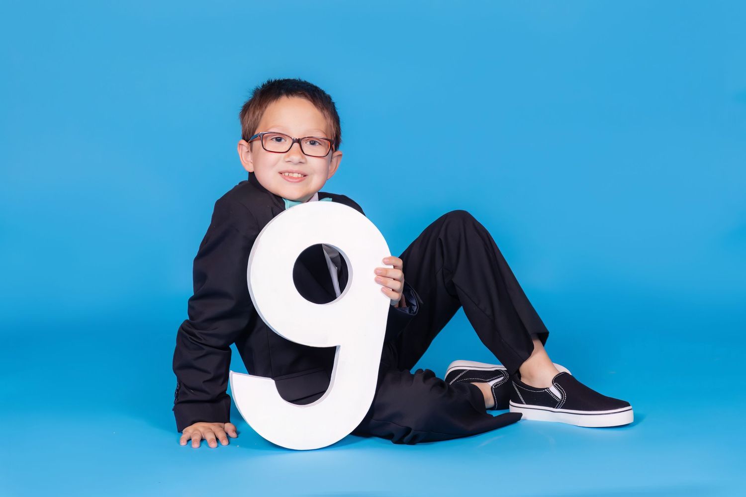 child sitting on floor holding a large 9 on solid savage blue jay backdrop in studio in clayton new jersey Gloucester