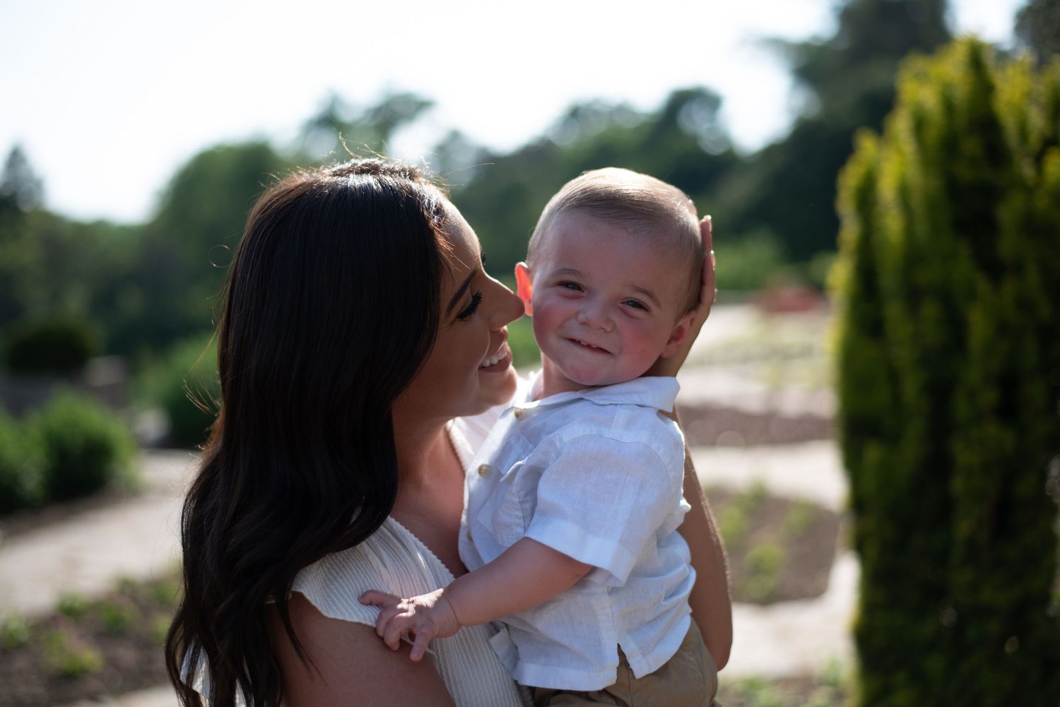 A tender moment captured between a parent and child outdoors with soft sunlit bokeh and greenery in the background.