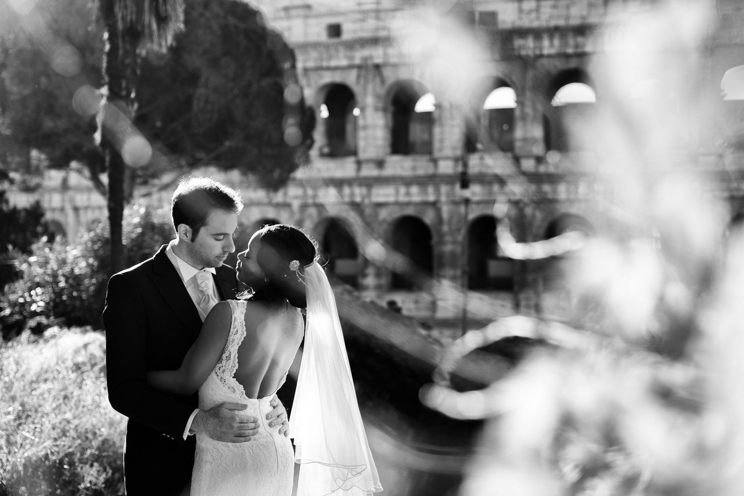Romantic wedding couple embraces in front of ornate stone architecture.