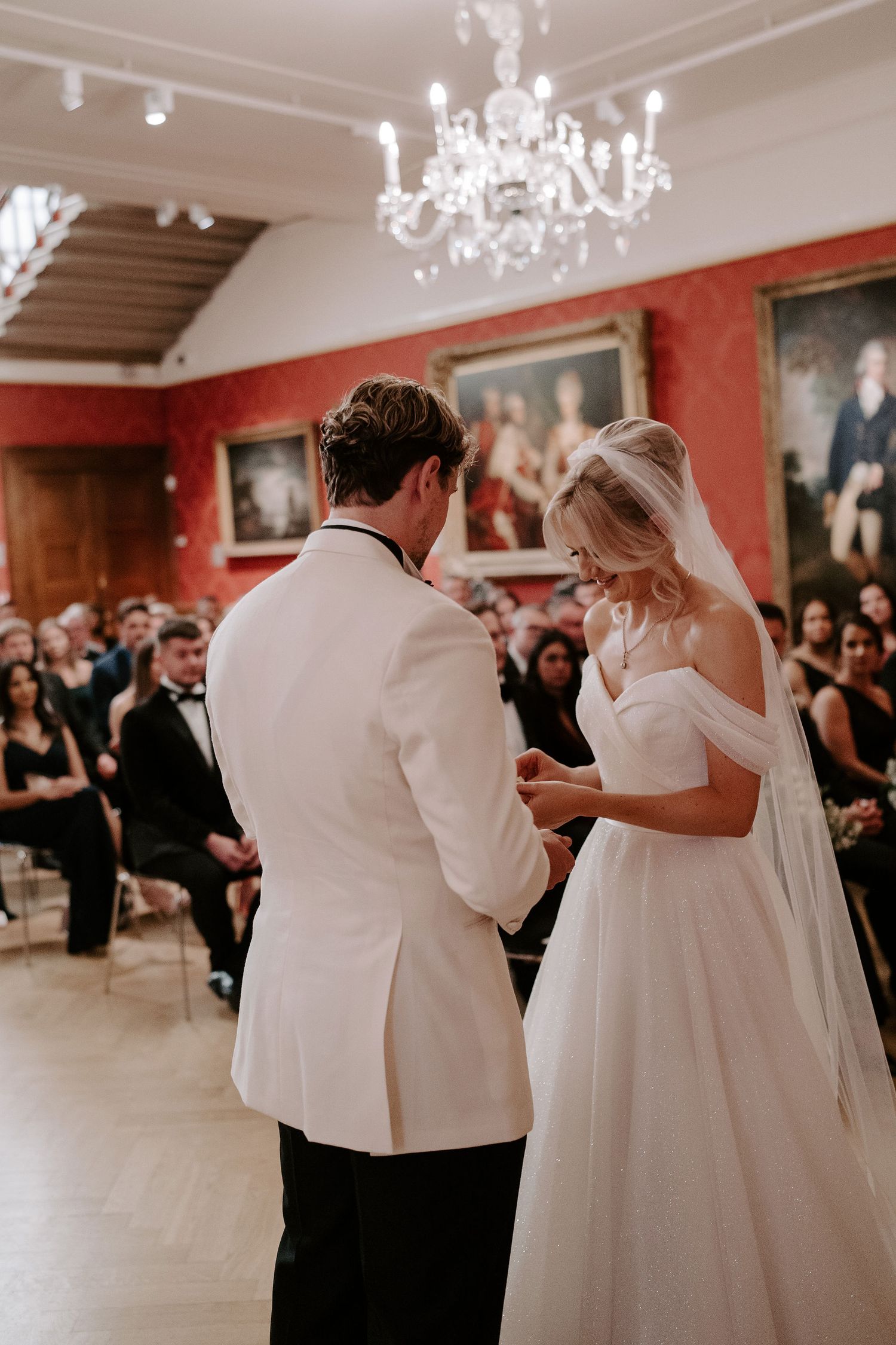 bride placing ring on grooms finger during ceremony in the European art gallery at the ashmolean museum