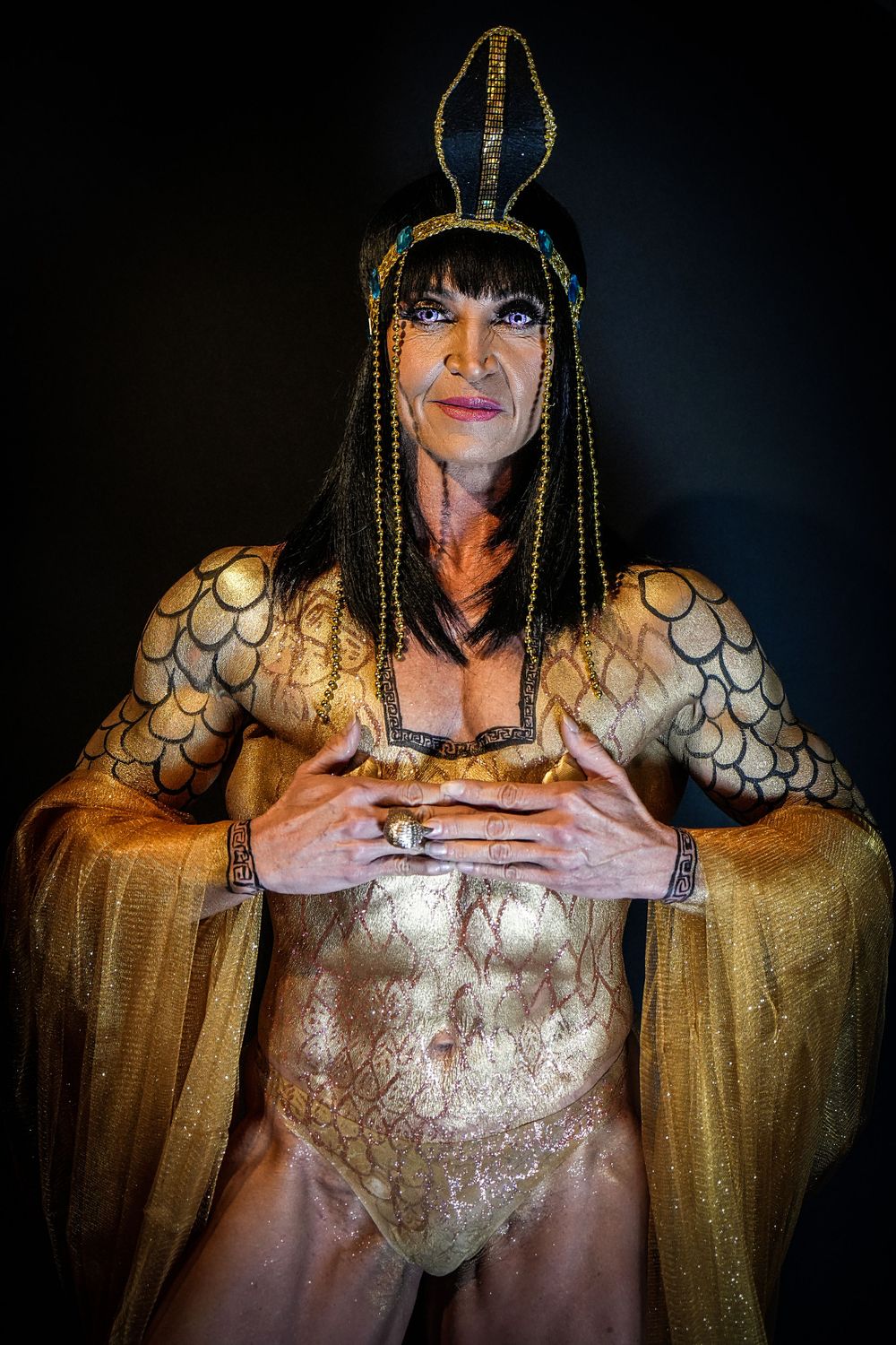 Theatrical performer in Egyptian-style golden costume with ornate headdress against dark background.