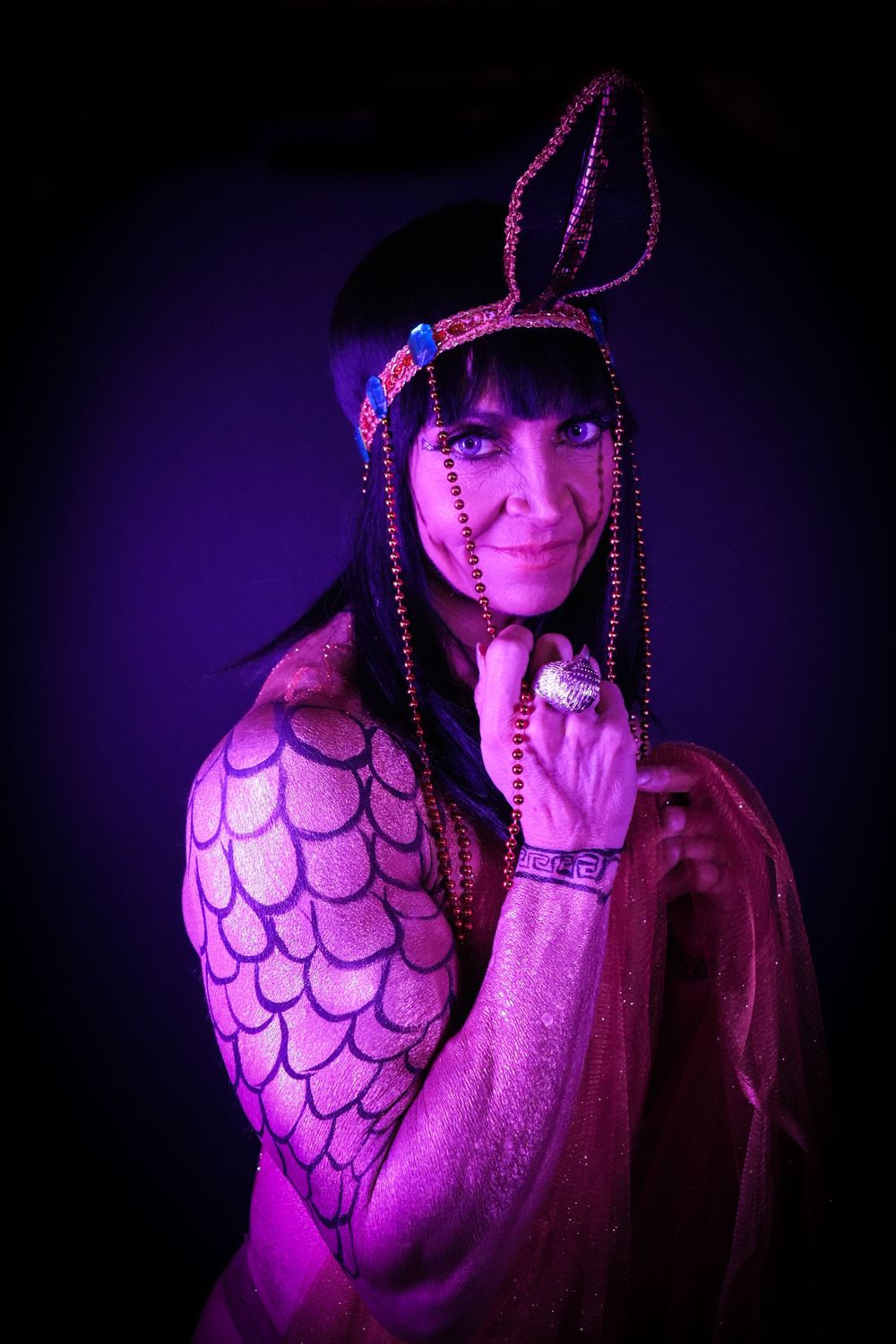 Theatrical portrait with purple lighting of performer in ornate costume and beaded headpiece.
