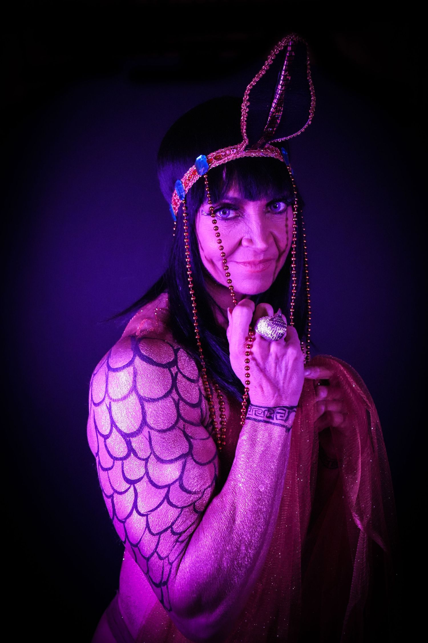 Theatrical portrait with purple lighting of performer in ornate costume and beaded headpiece.