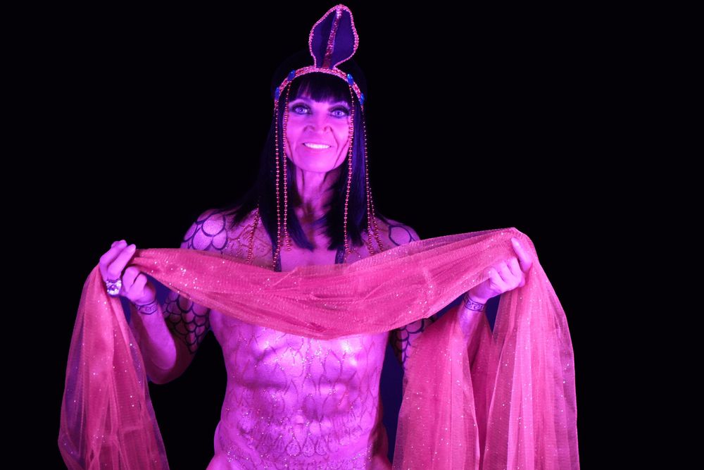 Performer in magenta lighting wearing decorative headdress and sheer costume.