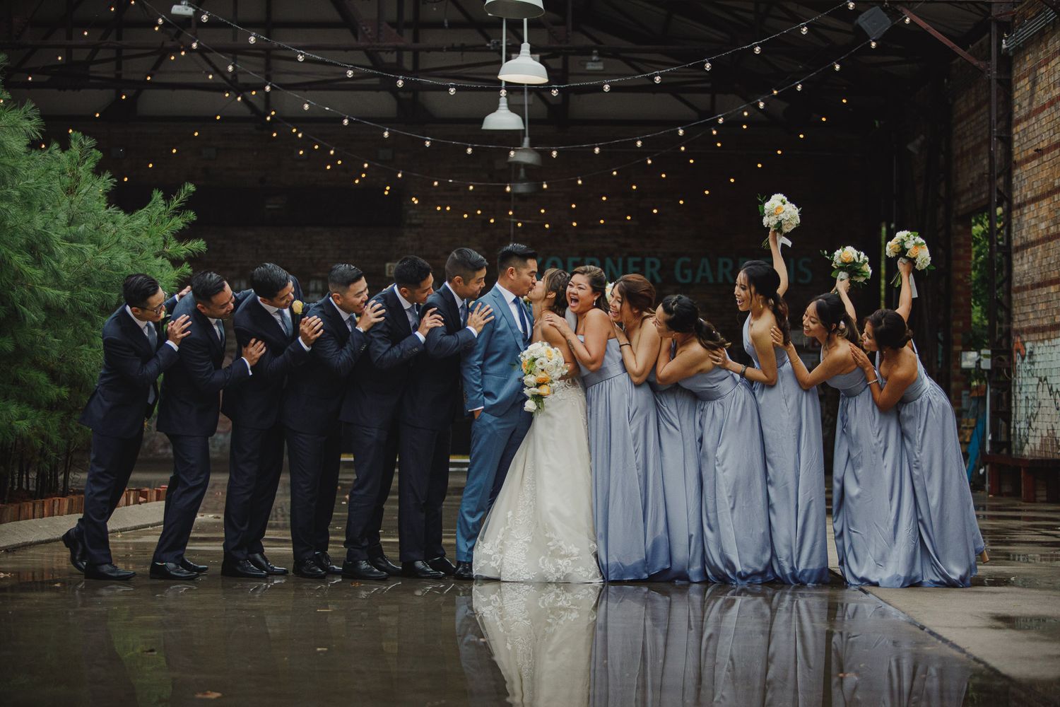 Wedding party poses in two rows with groomsmen in navy suits and bridesmaids in light blue dresses.