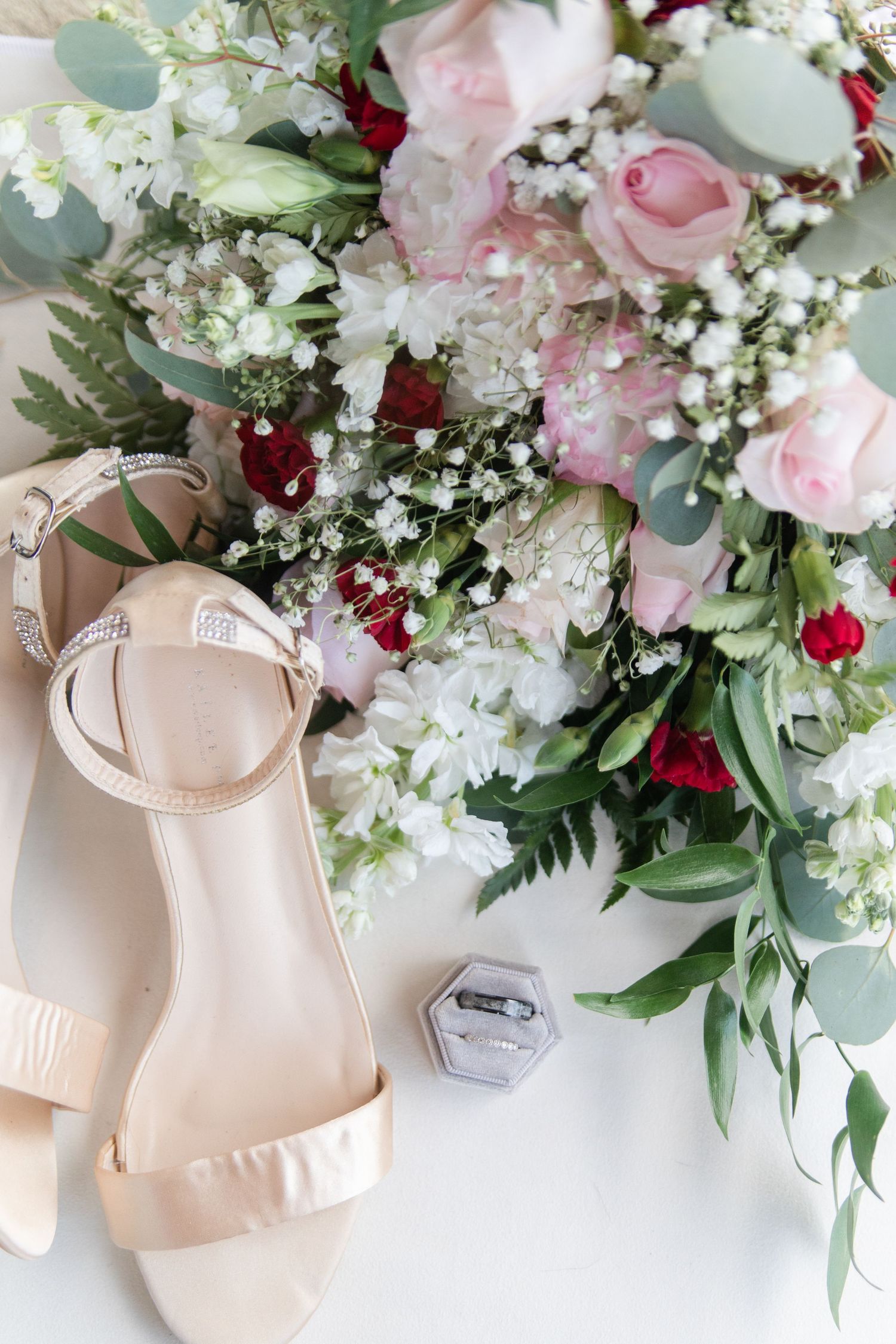 Wedding shoes and floral arrangements with pink roses and white flowers against a white background.