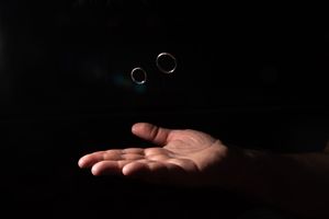Two wedding rings floating above an open hand against dark background.