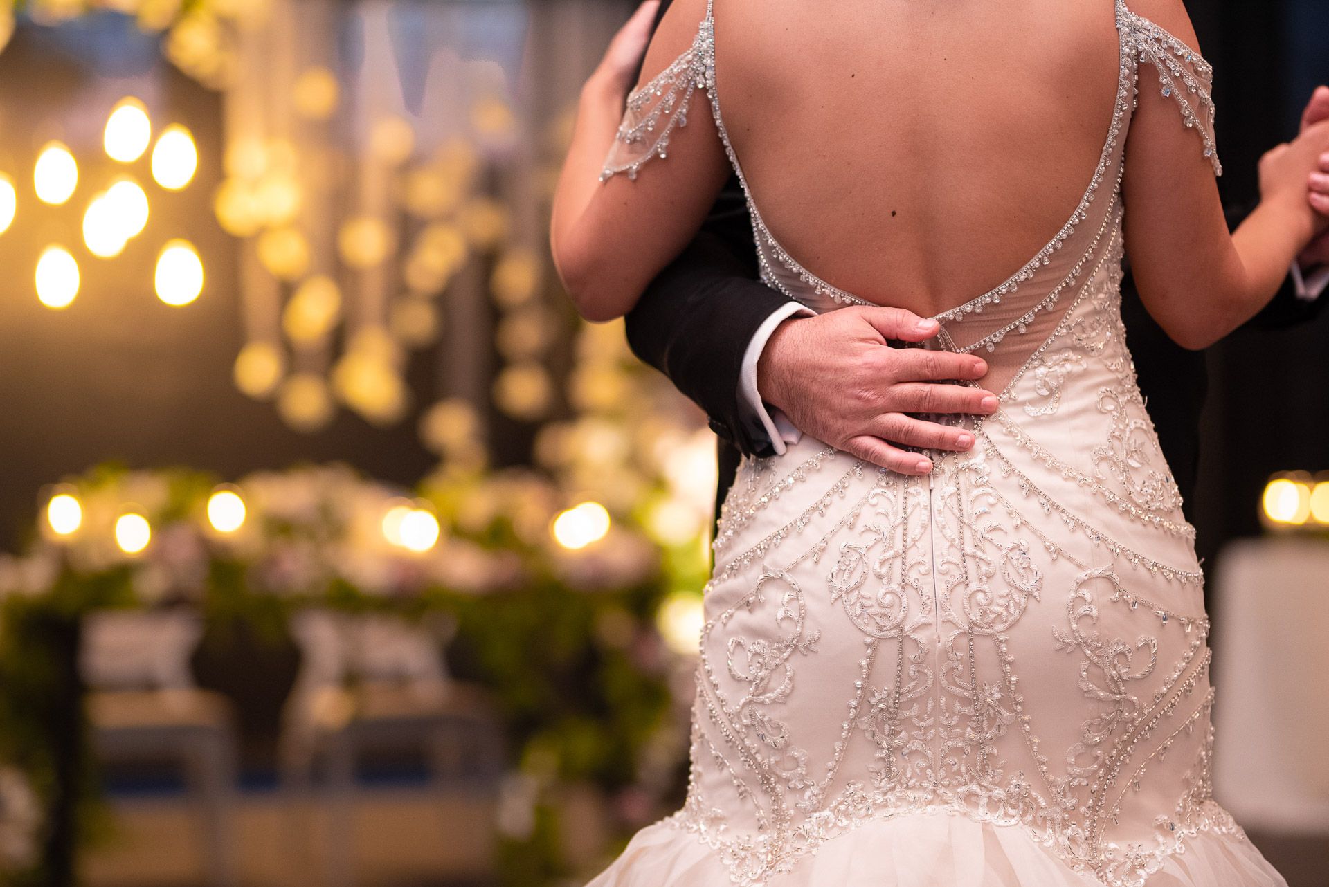 Close-up of bride in backless lace mermaid gown during first dance at romantic reception.