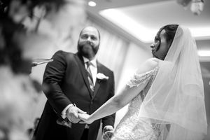Bride and groom hold hands during emotional wedding ceremony in black and white photography.