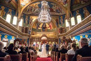 Elegant Orthodox church wedding ceremony with ornate golden iconostasis and chandelier.