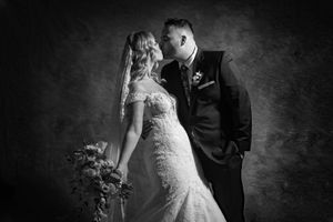 Bride and groom share a romantic kiss in elegant black and white studio wedding portrait.