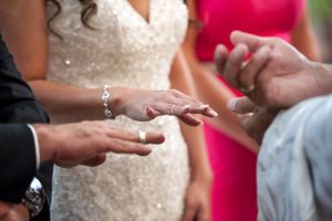 Close-up of wedding ring exchange ceremony with bride in beaded gown and pink bridesmaid nearby.