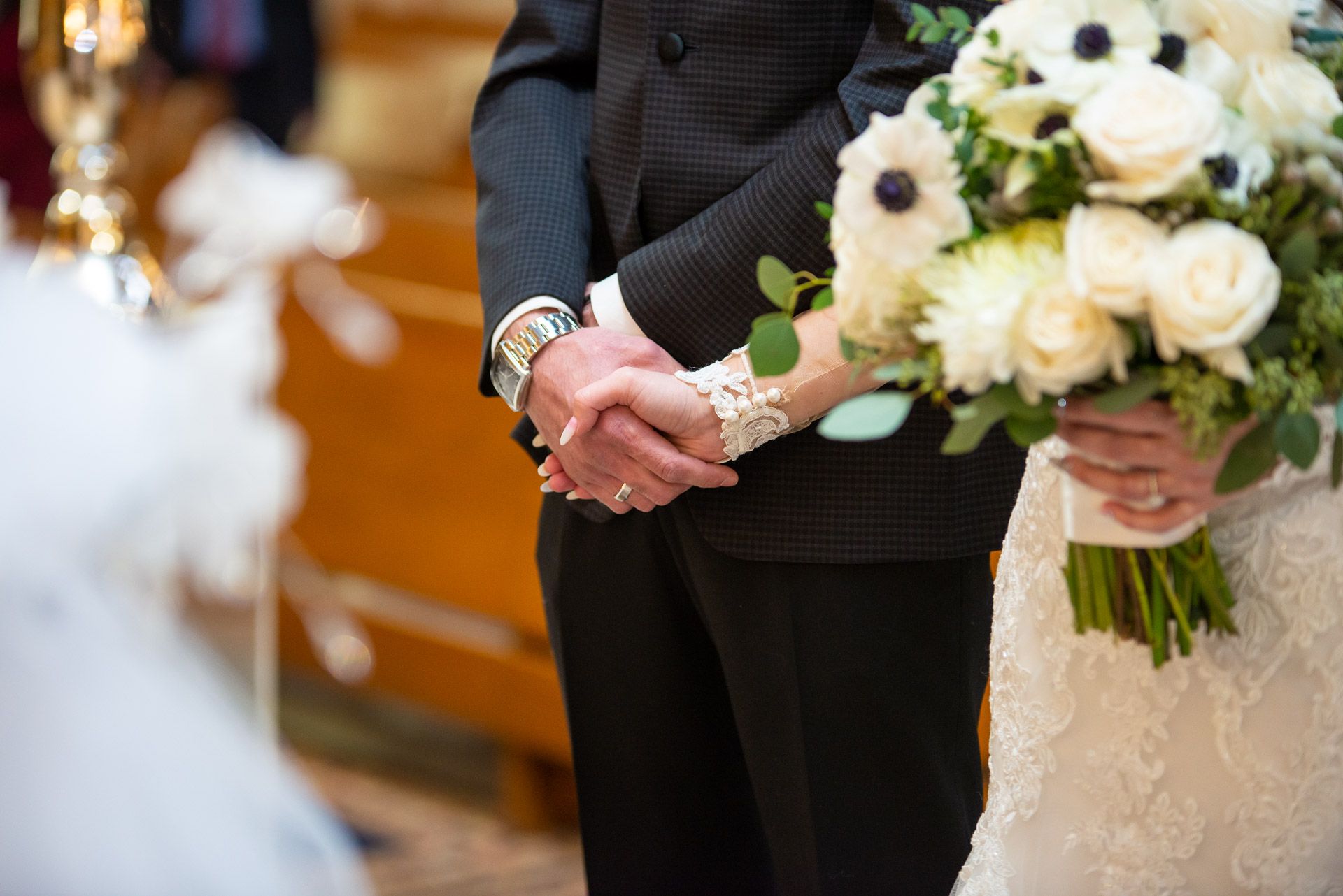 Bride and groom hold hands during wedding ceremony while bride holds white anemone bouquet.