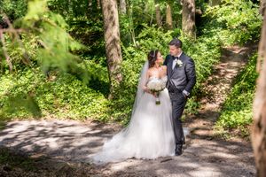 Bride and groom share intimate moment on sunlit forest path during wedding portraits.