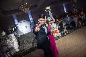 Groom points to camera while bride raises bouquet on wedding reception dance floor.