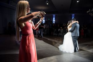 Violinist in pink gown serenades bride and groom during first dance at wedding.