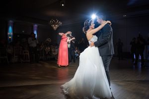 Bride and groom share first dance while violinist performs in elegant wedding reception ballroom.