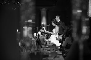 Bride and groom give speech at candlelit wedding reception in black and white photo.