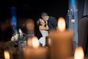 Bride and groom share romantic kiss surrounded by glowing candles at wedding reception.