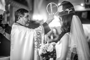 Black and white photo of Orthodox priest placing crowns on bride during wedding ceremony.