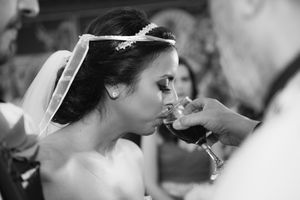 Bride drinks from ceremonial wine glass during traditional wedding ceremony in black and white.